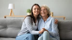 A senior woman and her daughter share a hug while sitting on a sofa