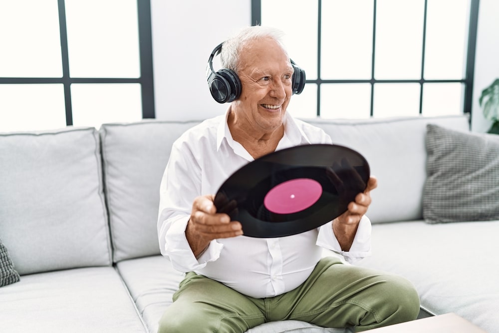 A senior man holding a vinyl record and listening to music on his headphones