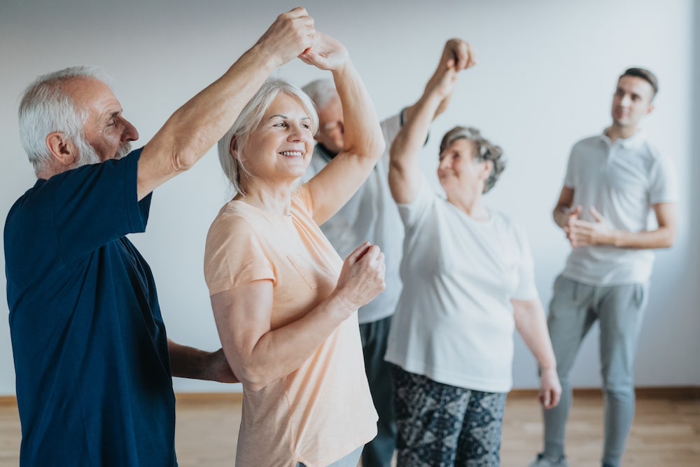 A group of senior friends taking a dance class at the best memory care in Iowa