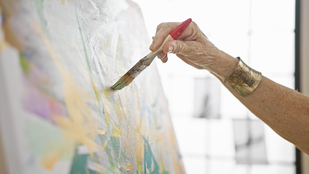 A senior woman painting flowers on canvas