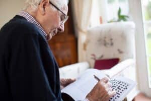 An older man doing a crossword puzzle as a part of the enrichment program available with Iowa dementia care services